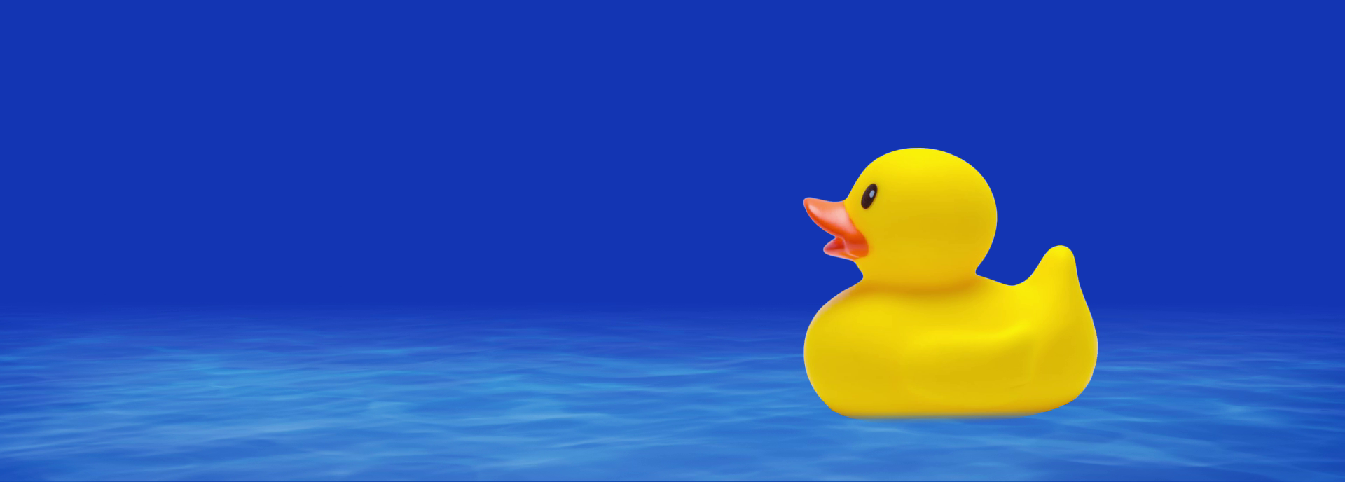 A yellow rubber duck floats calmly on a blue surface, resembling water, against a plain blue background, appearing slightly tilted with its beak open.