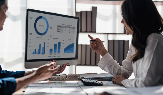 two people speaking and referencing a screen with different charts.